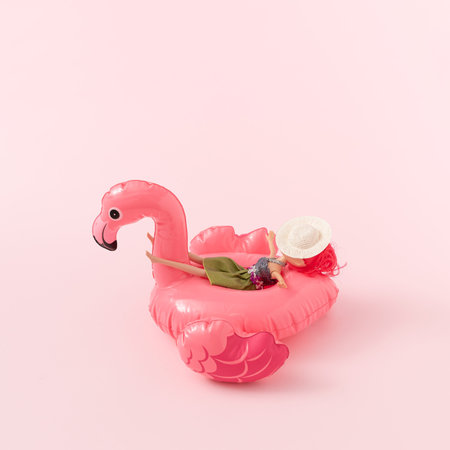 Minimal summer vacation scene made with pink flamingo rubber pool toy and doll against pastel pink...