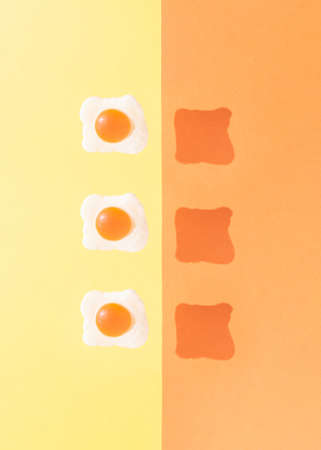 Three fried eggs with sunny day shadows against bright yellow and orange background. Minimal food concept. Creative breakfast idea.の写真素材