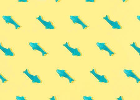 Summer pattern made with blue fish gummy candy on yellow background. Sunny day shadows. Flat lay.の写真素材