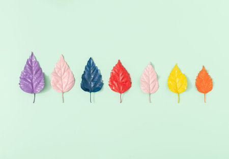 Colorful painted leaves on a pastel green background. Minimal nature layout. Autumn season concept.