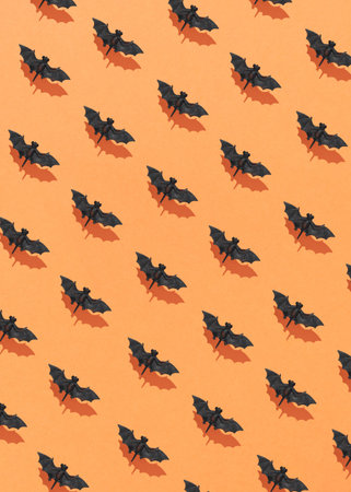 Halloween pattern made of flying bats with sunlight shadows against an orange background. Creative...