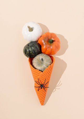 Orange ice cream cone with black spider and pumpkins with sunlight shadow on bright beige background. Creative Halloween concept. Minimal autumn holiday layout. Fun party food idea.の写真素材