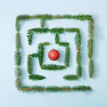 Natural maze made with fresh green fir branches and red Christmas bauble on bright blue background. ...