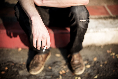 Hipster sitting and smoking cigarette on street sidewalkの写真素材