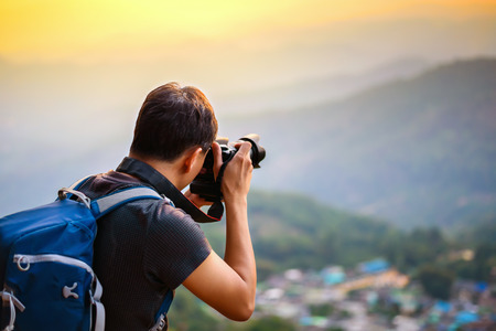 photographer tourist taking picture standing on top of the mountain in soft light of sunsetの写真素材