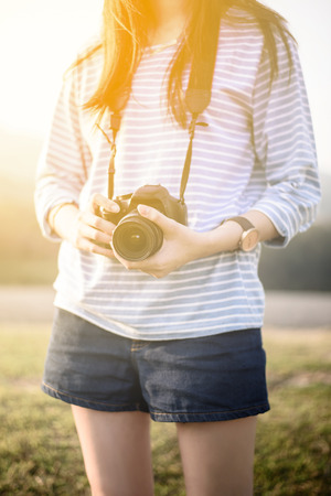 Asian girl holding camera outdoors in sunsetの写真素材