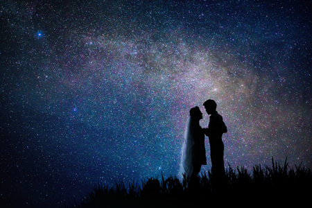 silhouette Romantic wedding couple holding hand on grass hill in milky way with stars field backgroundの写真素材