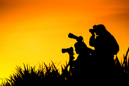 Silhouette of photographers group on grass hill in sunset eveningの写真素材