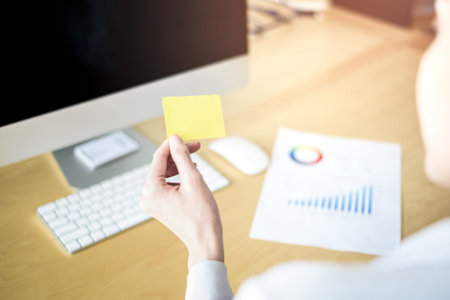 Business woman holding yellow sticky note on wooden table with desktop computer and document paper