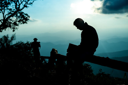 Silhouette of a man sitting and reading book on blue mountain peak