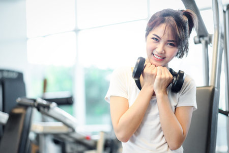 Happy beautiful asian woman smiling and lifting dumbbells cheerful in sports fitness gym , excersie...