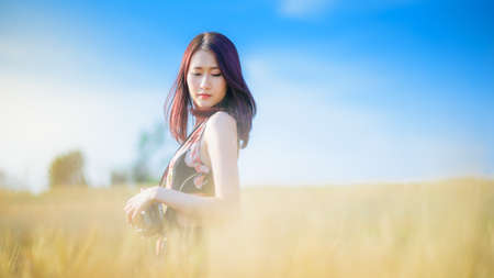 Charming asian woman Photographer holding camera on wheat summer fields in warm sunsetの写真素材