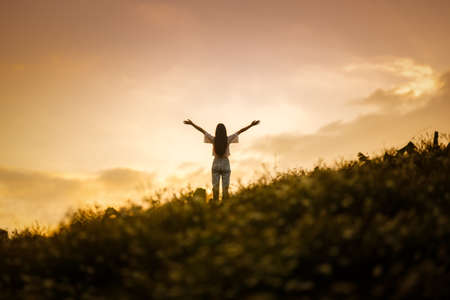 silhouette of happy woman relaxing on mountain hill  in summer sunset sky happy girl enjoying freedom and life raising arms feeling freeの写真素材