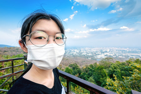 woman wearing surgical medical mask face protection on mountain view point over Chiang mai city , ...