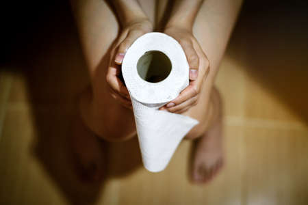 woman in towel holding toilet tissue paper roll in restroomの写真素材