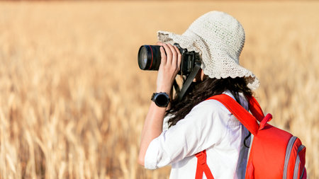 happy girl photographing ripe barley wheat field in soft light of sunset