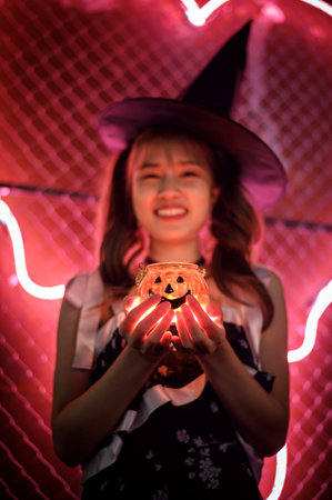 Little girl in halloween costume holding pumpkin lantern and smiling.