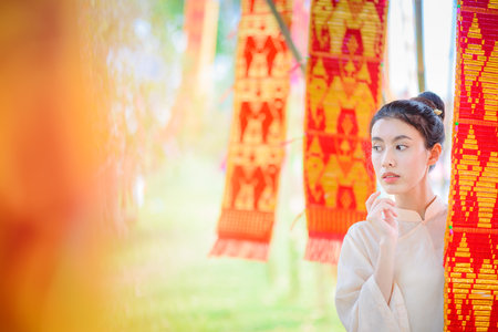 Beautiful smiling asian woman in traditional lanna style dress with colorful Lanna Tung flag, Chiang mai, Thailandの写真素材