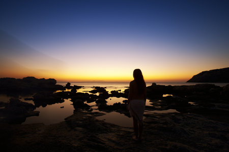 Beautiful young naked woman watching sunrise on Rhodes beach. Greek morning.
