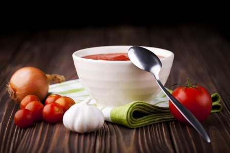 Fresh red tomato cream soup in white bowl. Dish and ingredients photography taken on old wooden table.の写真素材