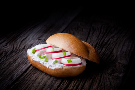 Delicious fresh baked roll  Bun sandwich served with creamy cottage cheese, spring onion and red radish slices  taken on old wooden table の写真素材