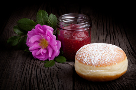 Fresh homemade donut covered by sugar powder frosting, wild rose flower and jar of red fruit jam. Sweets composition taken on rustic table.の写真素材