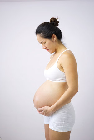 Happy asian chinese woman holding on her pregnant belly in photo studio