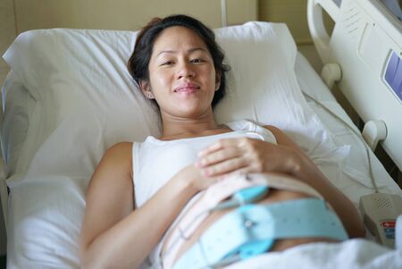 Pregnant Asian Chinese Woman lying on the hospital bed and waiting for the doctorの写真素材