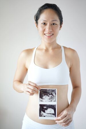 Delighted Happy Pregnant Asian Chinese holding the Ultra Sound Scan of her pregnancyの写真素材