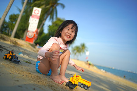 Single Asian chinese girl playing with earth-mover toys by the beach smilingの写真素材