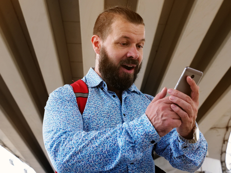 The bearded man got a message with good news on the phone. The man is reading the message on the phone in the street.の写真素材
