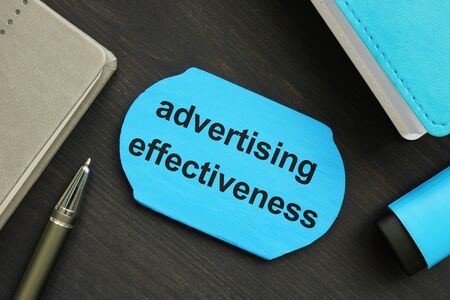 Writing note showing advertising effectiveness. The text is written on a small wooden blackboard. Markers, pen, wooden background are on the photo.の写真素材