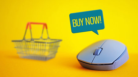 Online shopping concept. Buy now - online application offer home delivery. Shopping basket and computer mouse on the orange backgroundの写真素材