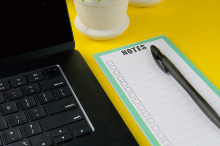 Workspace with laptop, notepad and black pen on bright yellow desk. Concept of planning,...