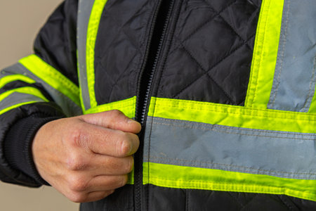 Close-up of a worker pointing at reflective tape on a high visibility jacket sleeve. Concept of workplace safety, protective clothing, industrial standards, and visibility at work.の写真素材
