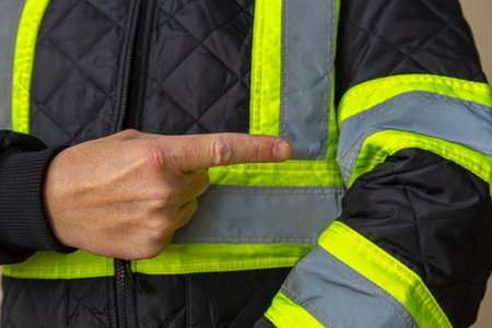 Close-up of a worker pointing at reflective tape on a high visibility jacket sleeve. Concept of workplace safety, protective clothing, industrial standards, and visibility at work.の写真素材