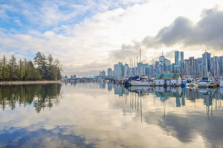 Calm marina with yachts and sailboats reflecting on still water, Vancouver city skyline in...