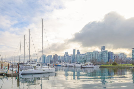 Vancouver Jan 1 2025. CanadaSkyliCalm marina with yachts and sailboats reflecting on still water, Vancouver city skyline in background, cloudy sky, peaceful urban waterfront scene.のeditorial素材