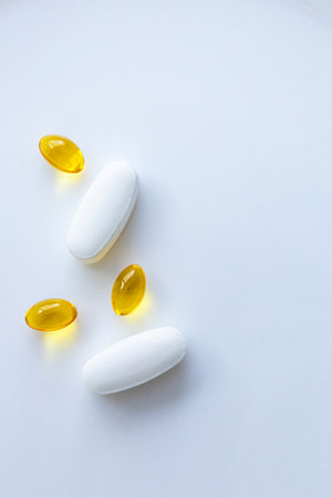 White tablets and yellow soft gel capsules on clean white background with copy space, minimal healthcare and supplement concept, top view flat lay.の写真素材