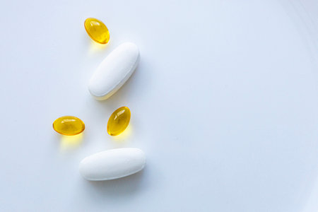 White tablets and yellow soft gel capsules on clean white background with copy space, minimal healthcare and supplement concept, top view flat lay.の写真素材