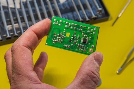 hand holding printed circuit board with microchip and soldered components on yellow background,...
