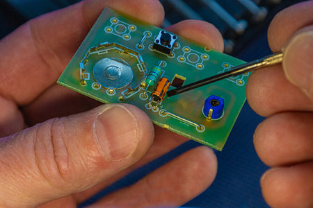Close up of hand holding printed circuit board with microchip and soldered components on yellow background, electronics repair and engineering concept.の写真素材
