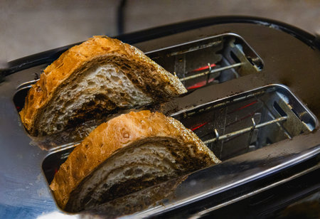 Closeup of rustic artisan bread halves inside a chrome toaster, ready for breakfast. Warm golden...