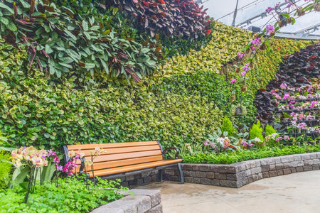 Wooden bench surrounded by dense green foliage, flowers, and ornamental plants in a landscaped...
