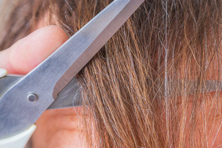 Macro close up of hairdresser scissors cutting brown hair near ear during haircut. Concept of...