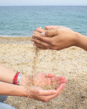 Hands playing with the sand on the beach, with the sea in the backgroundの写真素材