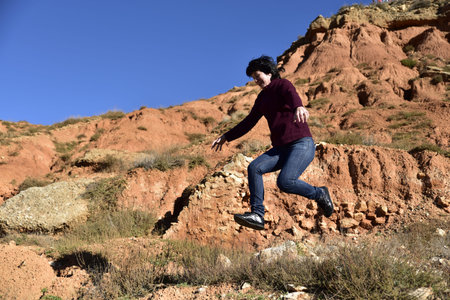 Young woman jumping on a cliff in the desert with red rocks.