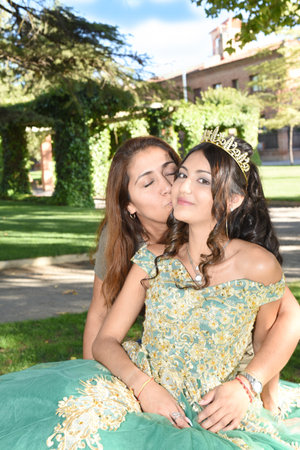 Mother giving a kiss to her 15-year-old daughter, wearing a green dress and a crownの写真素材