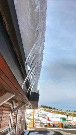 Icicles hanging from the roof of a wooden house in winterの写真素材