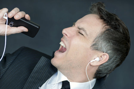 Close-up of a businessman wearing headohones singing into his cell phone.